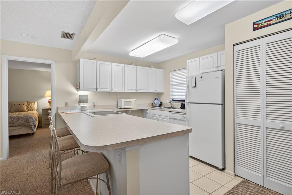 Kitchen featuring a kitchen bar, a peninsula, white appliances, white cabinetry, and light countertops