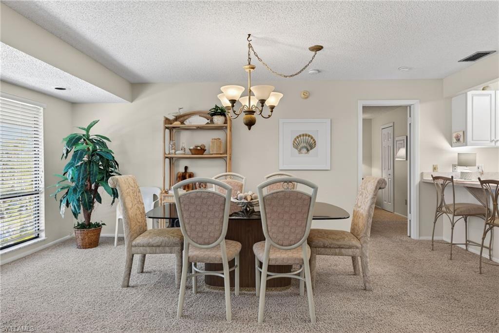 Dining area with light colored carpet, a textured ceiling, and a chandelier