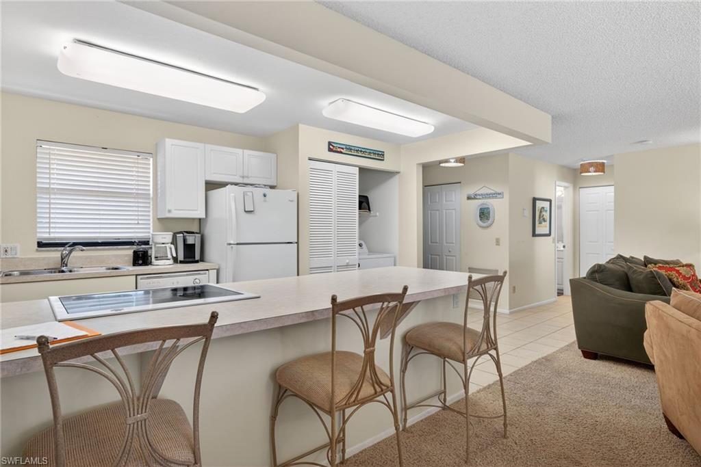 Kitchen with a breakfast bar area, light countertops, open floor plan, freestanding refrigerator, and white cabinetry