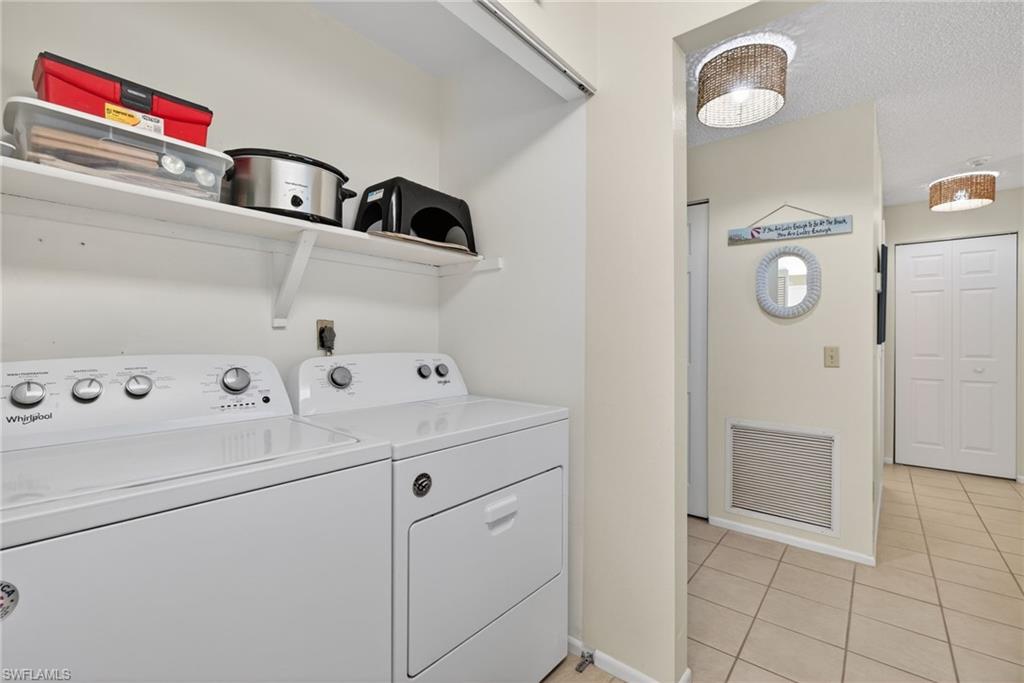 Laundry area featuring washer and clothes dryer, light tile patterned floors, and a textured ceiling