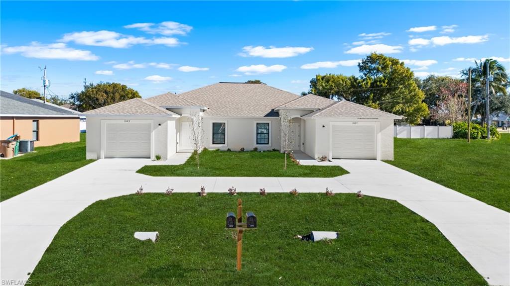 Contemporary duplex featuring a stucco exterior, twin single-car garages, separate paved driveways, a common front lawn, and individual covered entryways