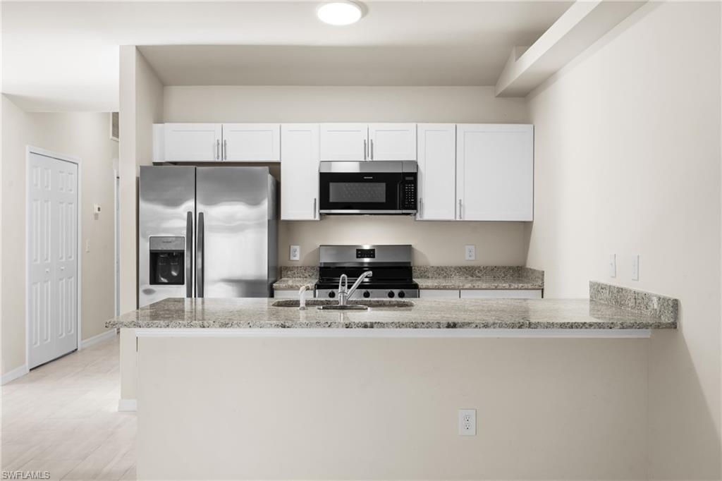 Open-concept kitchen featuring white cabinetry, stainless steel appliances, a double basin sink, and a spacious breakfast bar with stone countertops