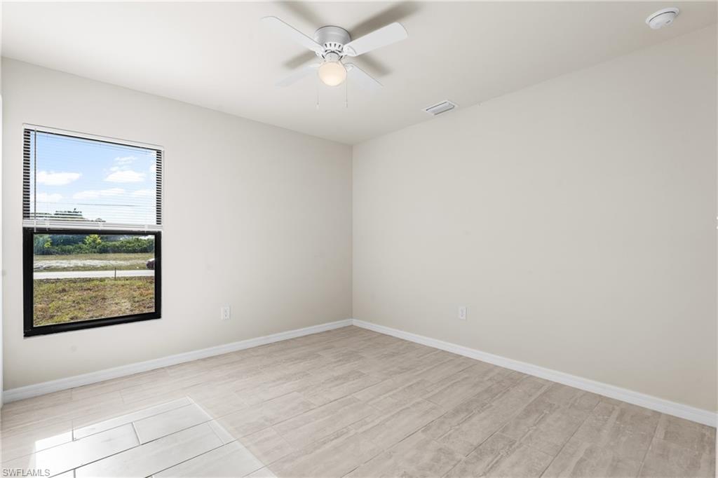Spacious room featuring wood-finish tile flooring, a large window with horizontal blinds, and a ceiling fan with integrated lighting