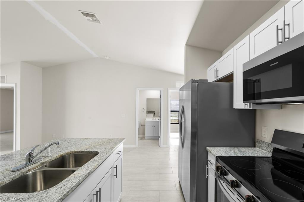 Kitchen featuring a dual basin sink, white cabinetry, granite-finish countertops, stainless steel refrigerator, and built-in microwave