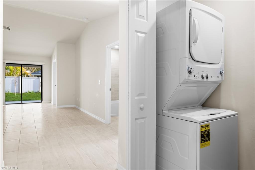 Stackable washer and dryer unit, light tile flooring, vaulted ceiling, white interior doors, and a sliding glass door to the exterior
