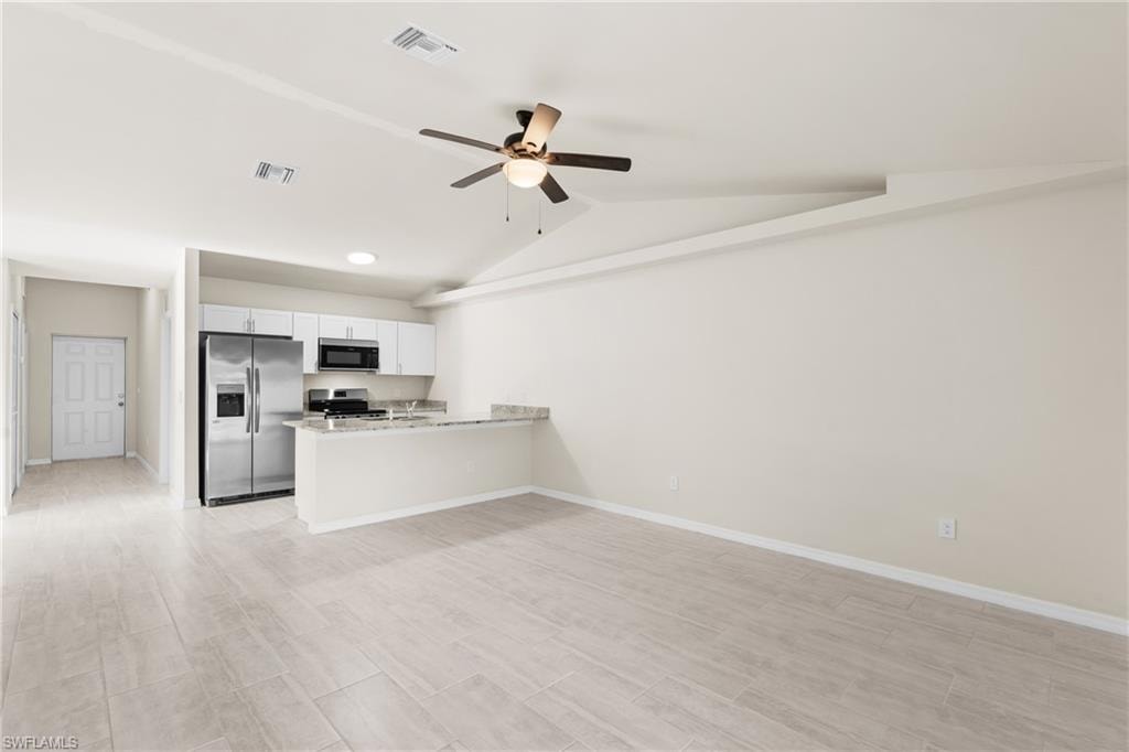 Open-concept living space with light-toned tile flooring, vaulted ceilings, and a ceiling fan