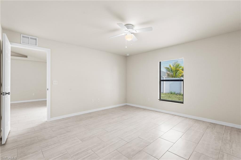 Spacious room featuring light-toned tile flooring, a single window with a dark frame, and a ceiling fan with integrated lighting