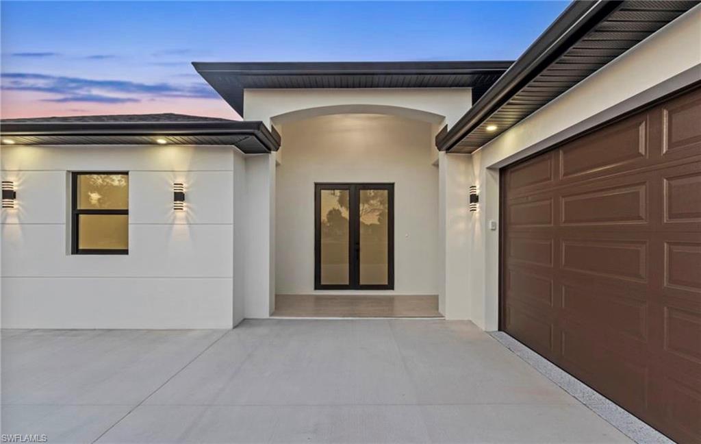 Modern exterior featuring a two-car garage with an epoxy-finished floor, contemporary wall sconces, dark-framed windows, and a sliding glass entry door