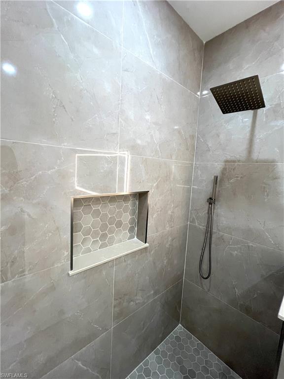 Tiled shower enclosure featuring light grey marble-look wall tiles, a built-in niche with hexagonal tile backing, and a dark-toned square rainfall showerhead