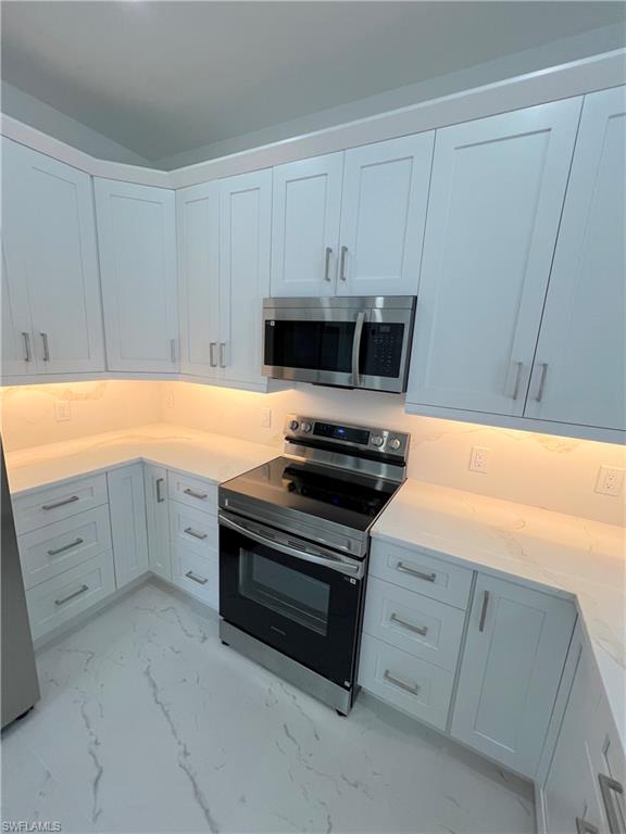 Modern kitchen featuring white shaker-style cabinetry, stainless steel appliances, and under-cabinet lighting