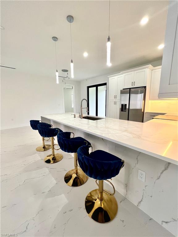 Spacious kitchen featuring a large island with a waterfall countertop, white cabinetry, stainless steel appliances, and recessed lighting