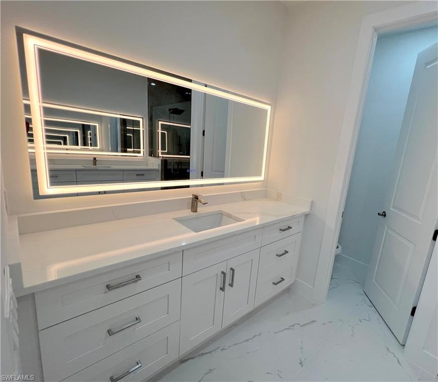 Backlit vanity mirror illuminating a spacious white vanity with an integrated sink, polished chrome faucet, and ample storage cabinetry