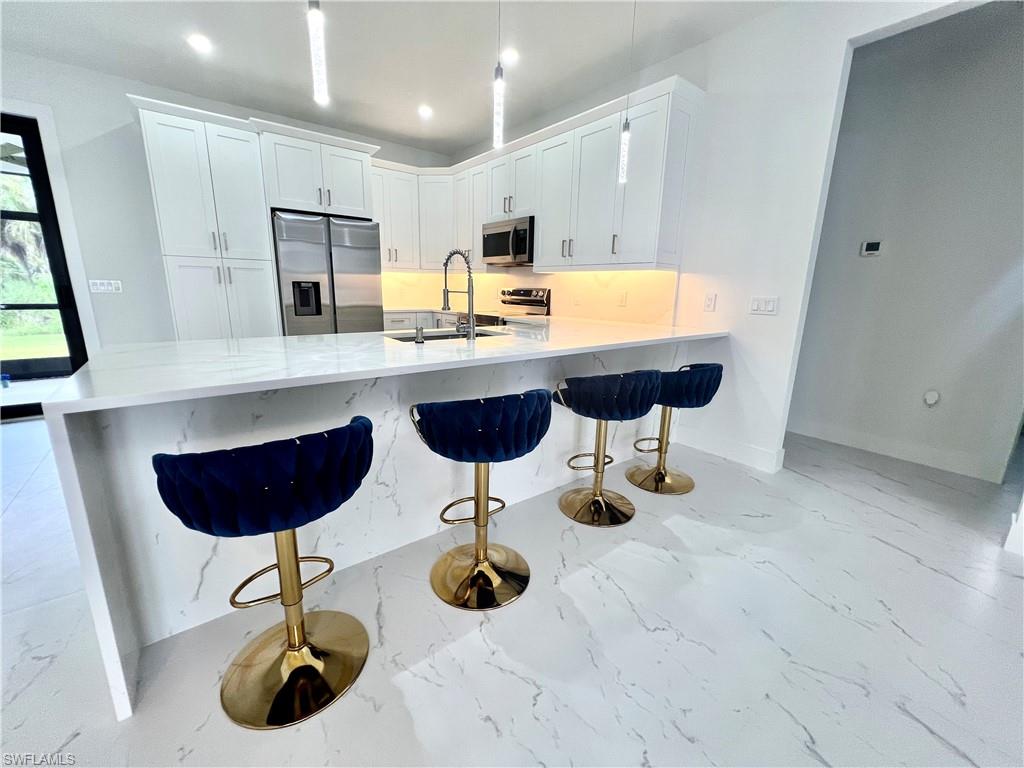 Modern kitchen featuring white shaker cabinetry, stainless steel appliances, a waterfall island with a quartz countertop, and large format marble-look tile flooring