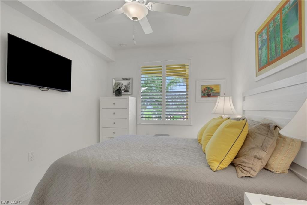 Bedroom featuring a wall-mounted television, ceiling fan, and window with plantation shutters