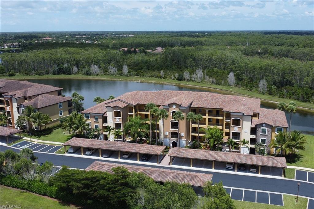 Lakeside condominium building featuring multi-story construction, covered parking, mature palm trees, and terracotta-style roof tiles