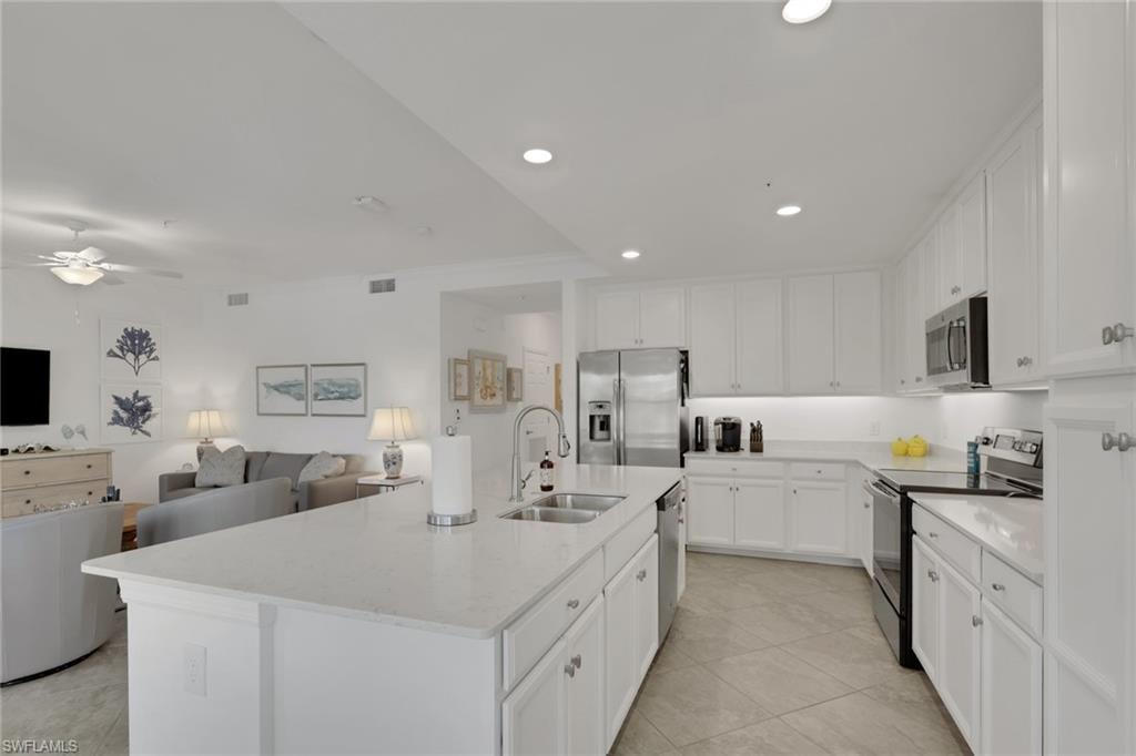 Gourmet kitchen featuring a large center island with double basin sink, white cabinetry with silver hardware, stainless steel appliances, and integrated recessed lighting