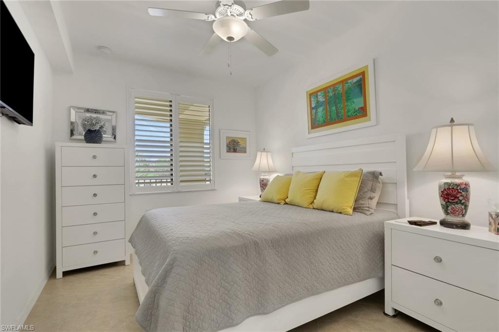Bright bedroom featuring a white paneled headboard, plantation shutters, a ceiling fan with integrated lighting, and neutral wall-to-wall carpeting