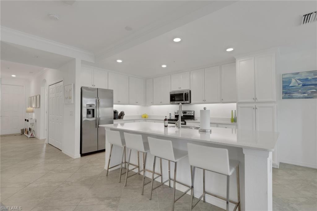 Modern kitchen featuring extensive white cabinetry, stainless steel appliances, and a large central island with seating