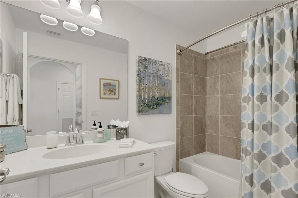 Full bathroom featuring a white vanity with an integrated sink, a large wall-mounted mirror, and a built-in tub with tile surround