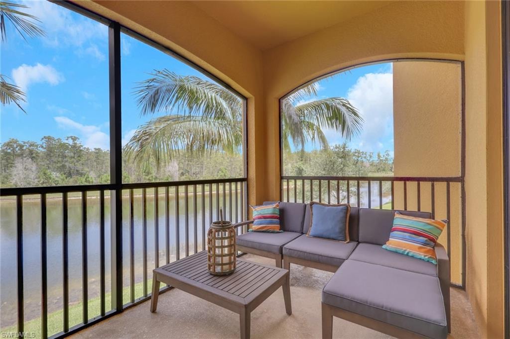 Screened balcony featuring arched openings, a water backdrop, tropical foliage, and an outdoor patio surface