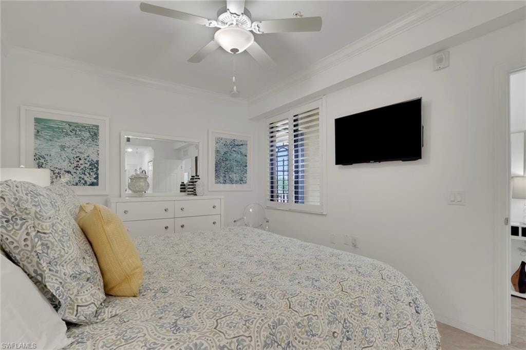 Bedroom featuring a ceiling fan with integrated lighting, crown molding, and plantation shutters