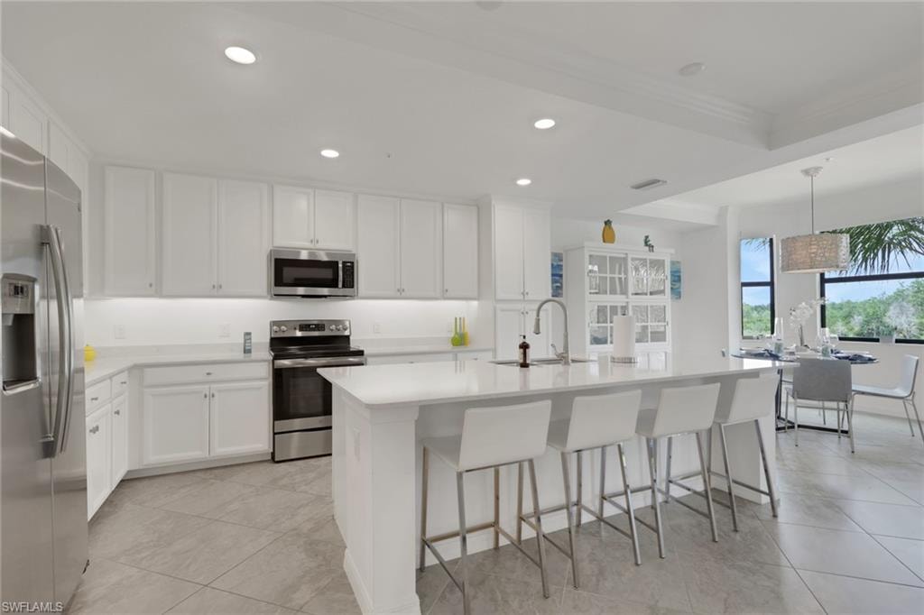 Modern kitchen featuring white cabinetry, stainless steel appliances, a center island with seating, a white solid surface countertop, and large format tile flooring