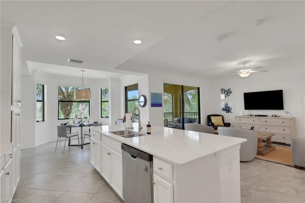 Open-concept kitchen featuring an island with a double basin sink, stainless steel dishwasher, and white cabinetry