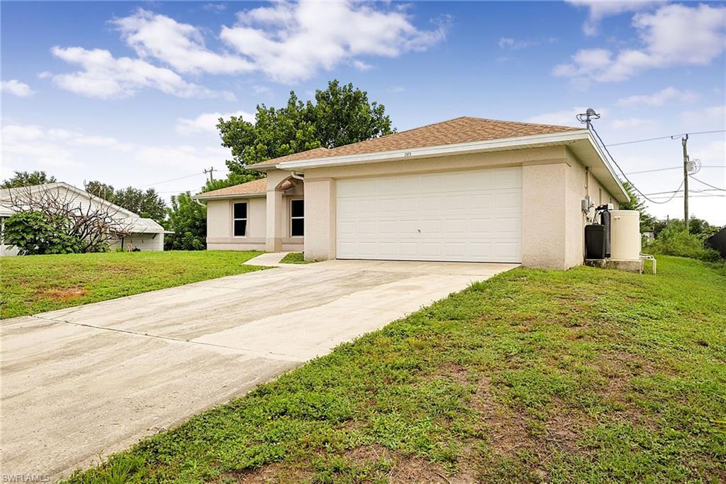 Cream stucco exterior featuring a two-car garage, concrete driveway, and brown shingle roof