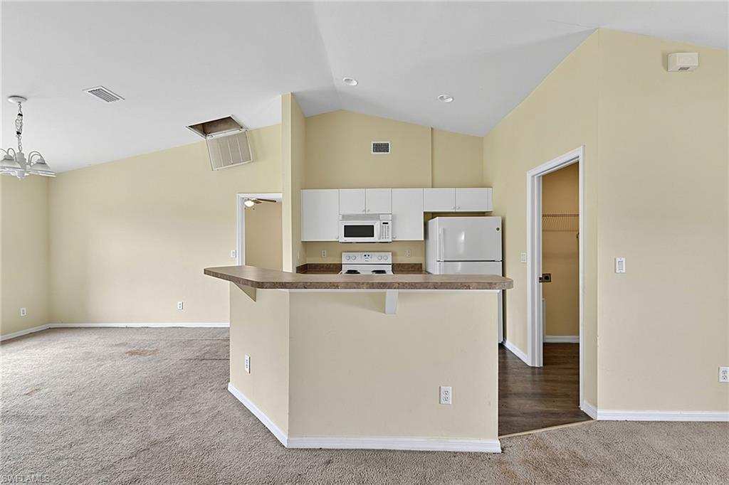 Open-concept kitchen and living area featuring vaulted ceilings, a breakfast bar with a laminate countertop, white cabinetry, and white appliances