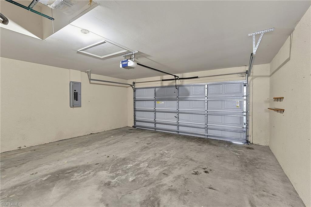 Spacious garage featuring a concrete floor, an automatic garage door opener, an electrical service panel, an attic access panel, and built-in shelving