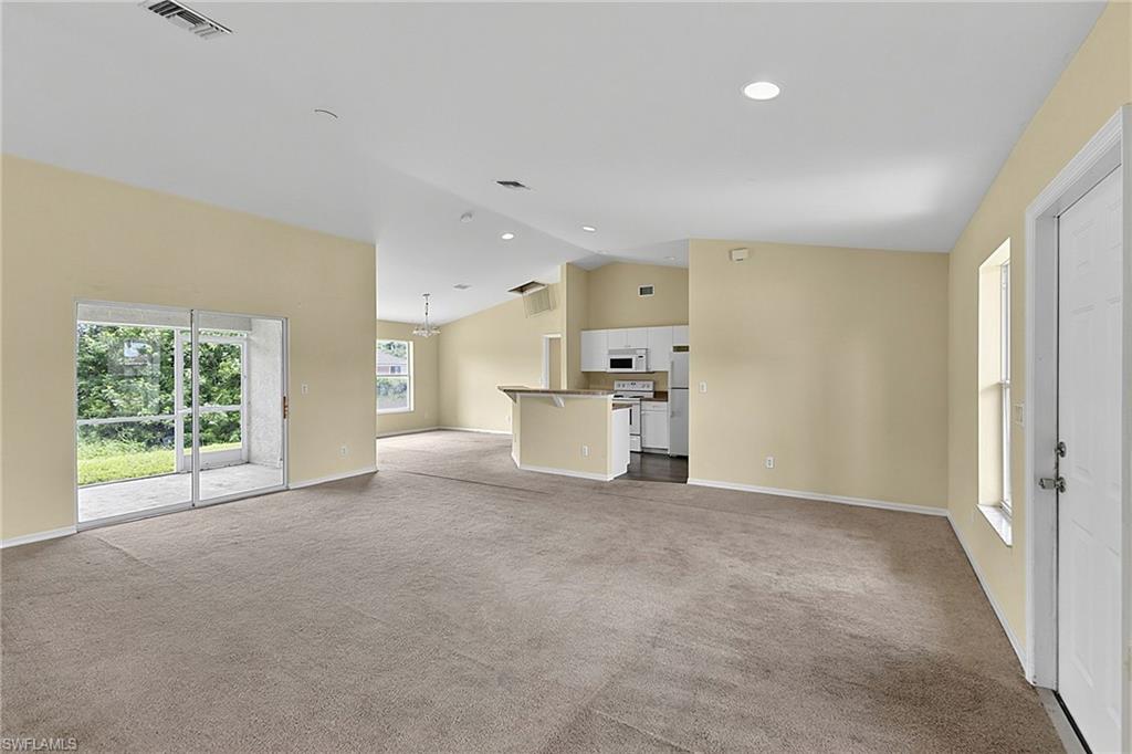 Expansive living area with neutral carpeting, vaulted ceilings, and a sliding glass door leading to a screened patio
