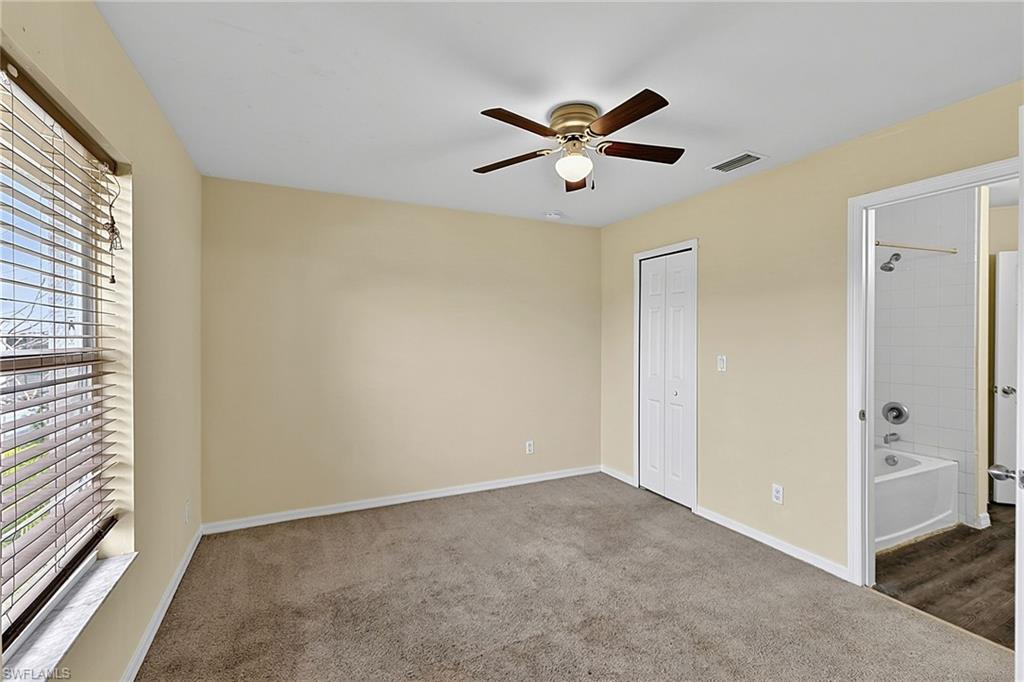 Carpeted room featuring a ceiling fan with integrated lighting, a window with horizontal blinds, a bi-fold closet door, and access to a bathroom with a tiled shower-bathtub combination