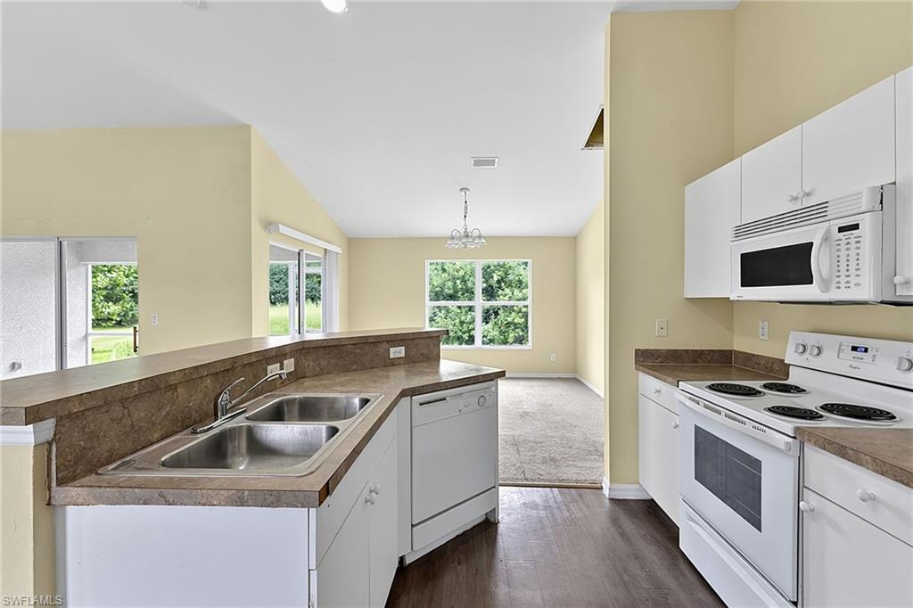 Kitchen featuring wood-finish flooring, white cabinetry, brown countertops, a double basin stainless steel sink, and white appliances including a microwave, dishwasher, and range