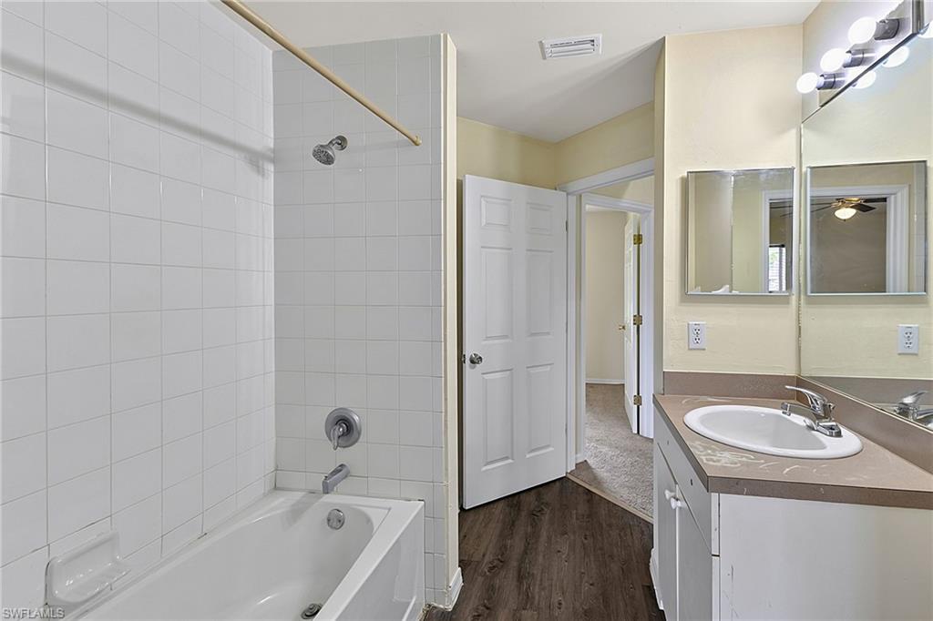Bathroom featuring a white bathtub with subway tile surround, a single vanity with an integrated sink and light-toned countertop, and dark wood-finish flooring