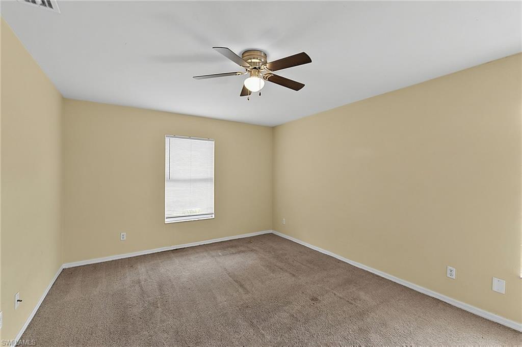 Spacious room featuring neutral carpeting, light beige walls, a window with horizontal blinds, and a ceiling fan with integrated lighting