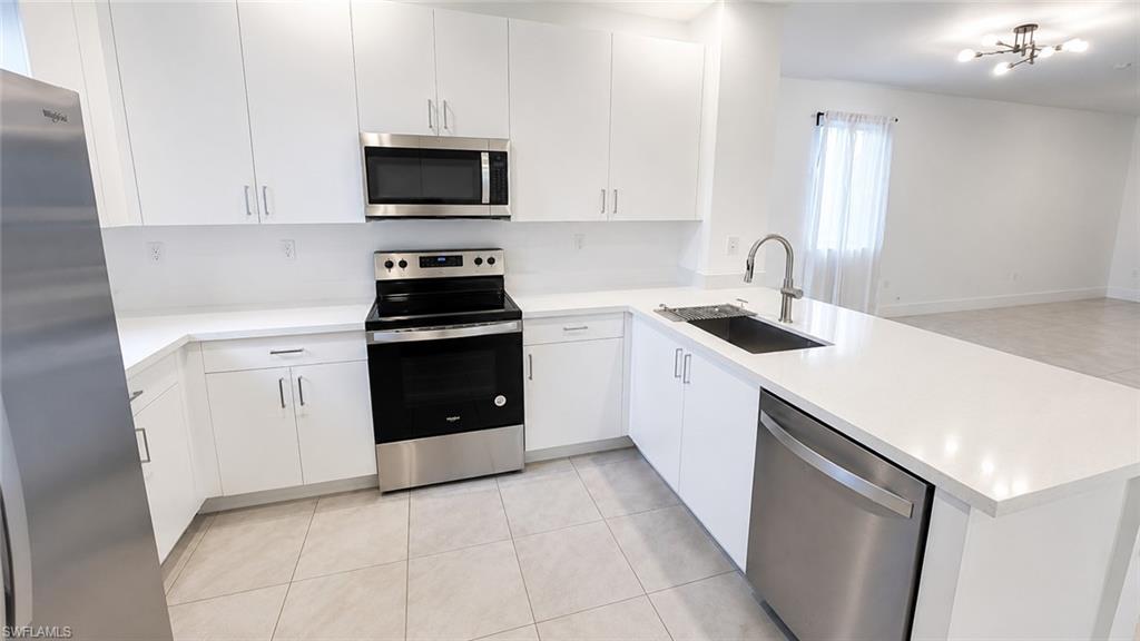 Modern kitchen featuring white cabinetry, stainless steel appliances, a deep basin sink with a gooseneck faucet, light-toned countertop, and tile flooring