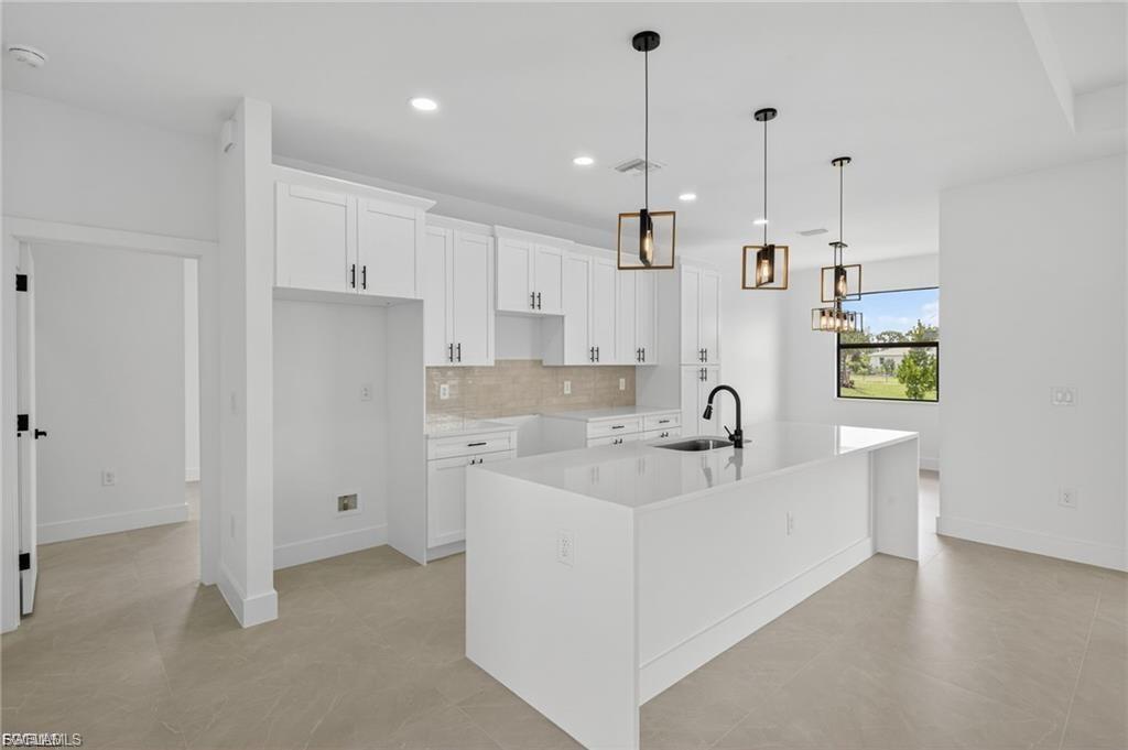 Modern kitchen featuring a large center island with integrated sink, white shaker cabinetry, tiled backsplash, and matte black fixtures
