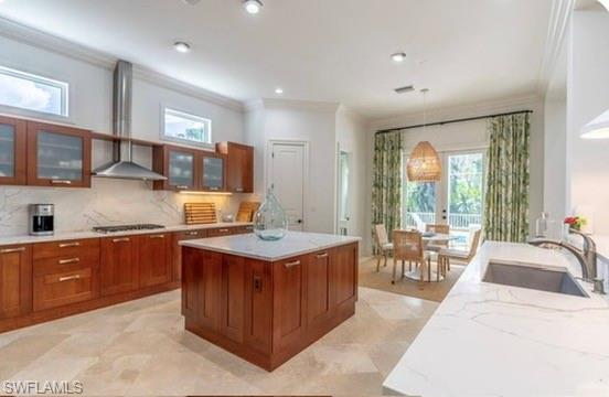 Kitchen featuring glass insert cabinets, ornamental molding, a center island, wood finish cabinetry, and pendant lighting