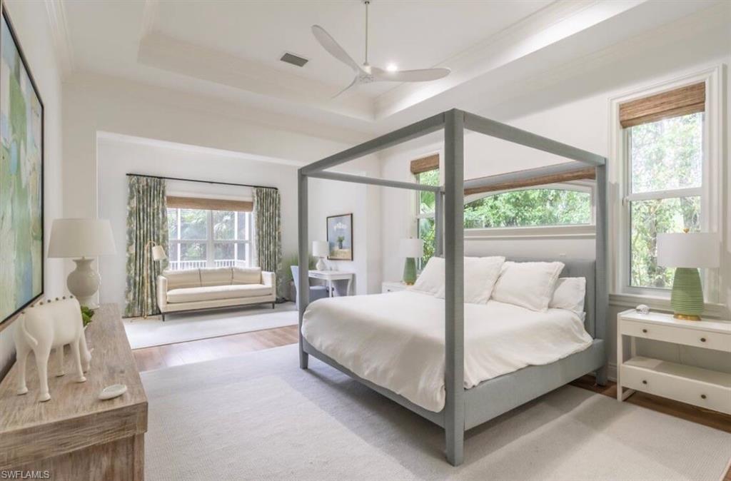 Bedroom with light wood finished floors, a ceiling fan, a tray ceiling, and crown molding
