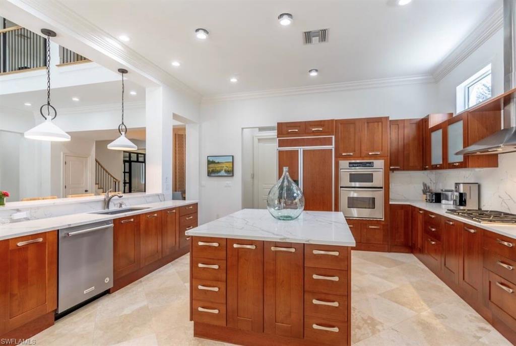 Kitchen with light stone counters, a kitchen island, stainless steel appliances, wood finish cabinetry, and pendant lighting