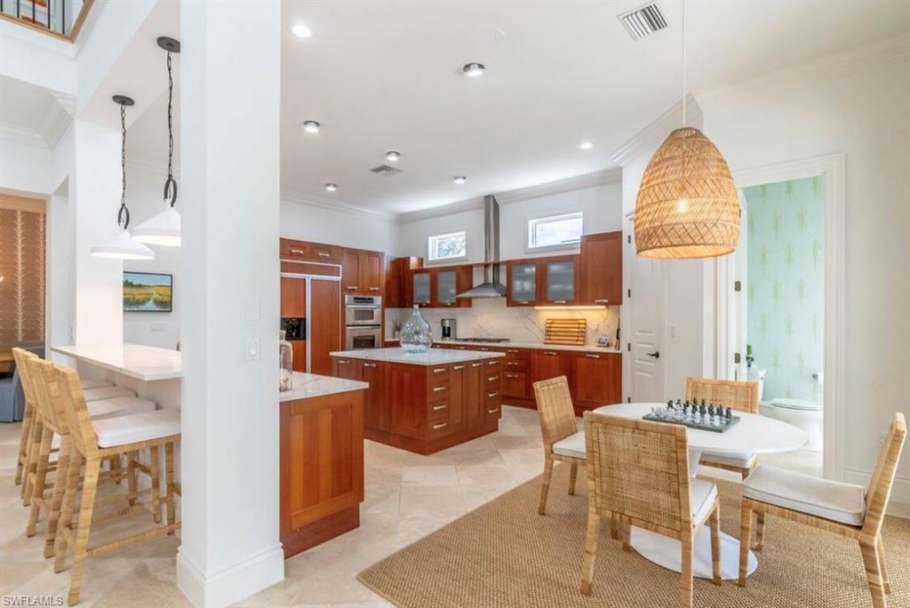 Kitchen featuring ornamental molding, decorative light fixtures, wood finish cabinets, glass fronted cabinets, and light stone countertops