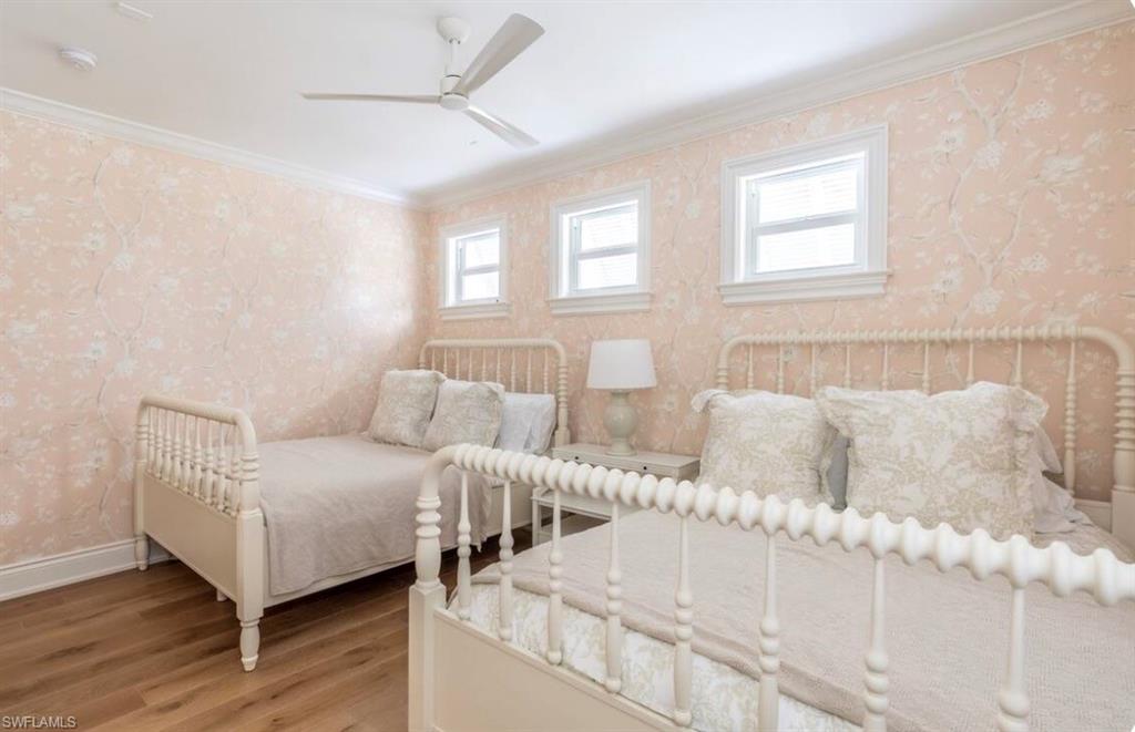 Bedroom featuring wallpapered walls, wood finished floors, ornamental molding, and a ceiling fan