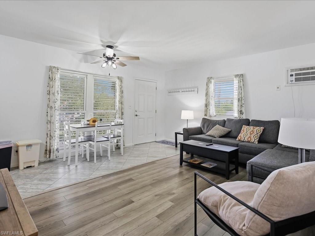 Open-concept room featuring wood-finish flooring, a ceiling fan with integrated lighting, and multiple windows with horizontal blinds