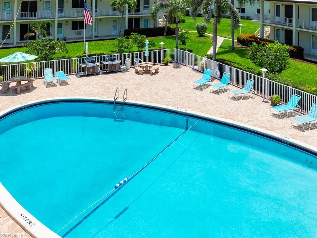 Resort-style pool area with a spacious paver deck, white perimeter fencing, and manicured green spaces