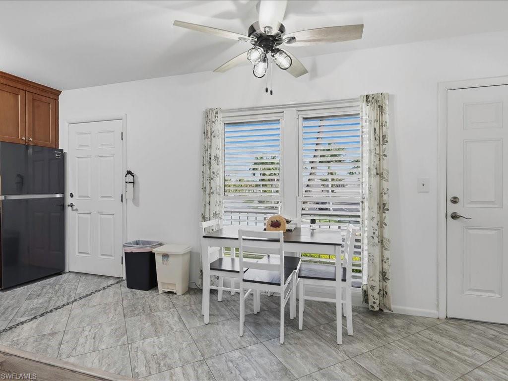 Kitchen area featuring light gray tile flooring with a dark accent border, double windows with horizontal blinds, overhead cabinetry, and a ceiling fan with integrated lighting