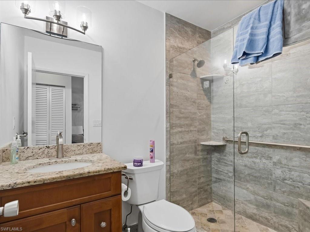 Bathroom featuring a frameless glass shower enclosure, wood vanity with granite countertop, undermount sink, and brushed nickel fixtures