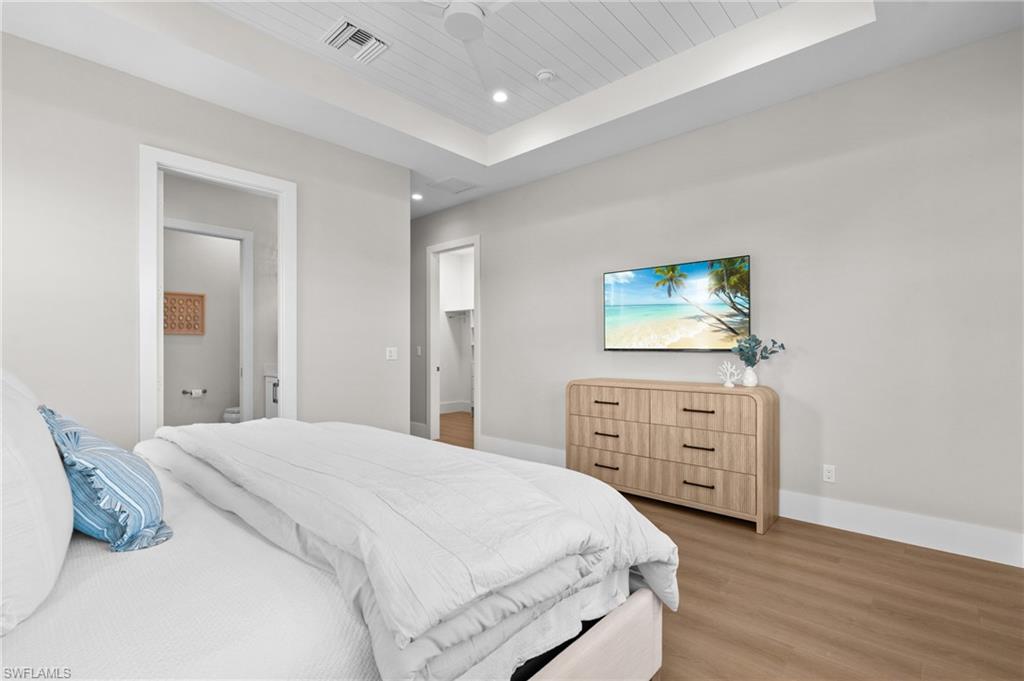 Bedroom with a raised ceiling, wooden ceiling, light wood-type flooring, and baseboards. virtually edited photo
