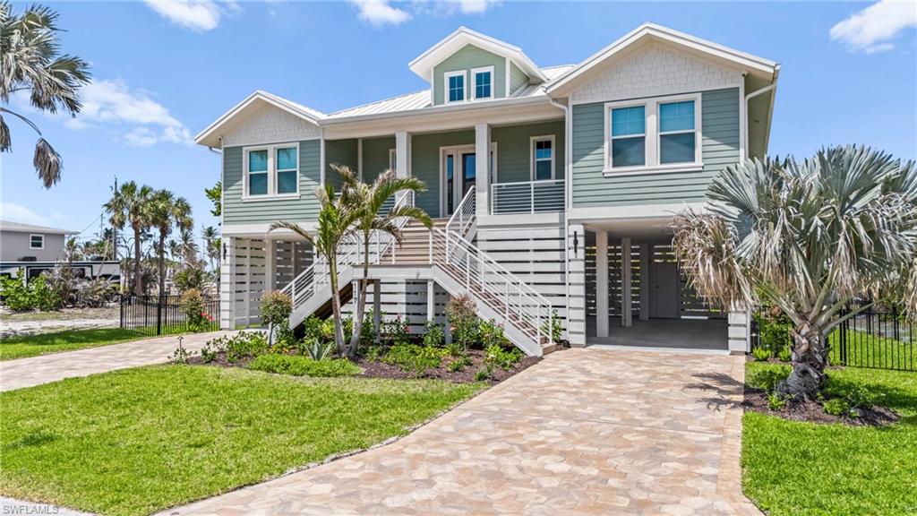 Coastal inspired home with stairway, driveway, a carport, covered porch, and a front yard. virtually edited photo