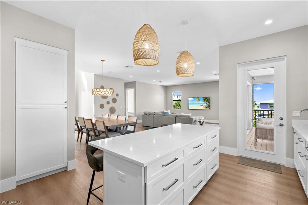 Kitchen with light wood-type flooring, recessed lighting, white cabinetry, a breakfast bar area, and hanging light fixtures. virtually edited photo