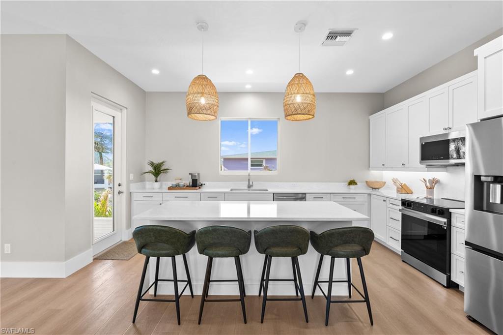 Entertainers Kitchen with a sink, stainless steel appliances, light wood finished floors, a kitchen bar, and visible vents - virtually edited photo
